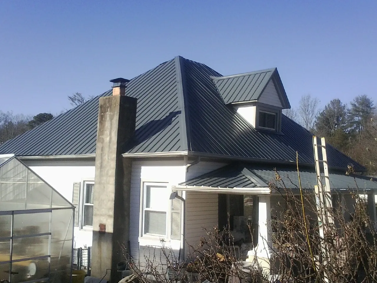 Dark blue standing seam metal roof on a white farmhouse with dormer — Slate & Tile Roof Repair by Roofing Brothers in Bullard