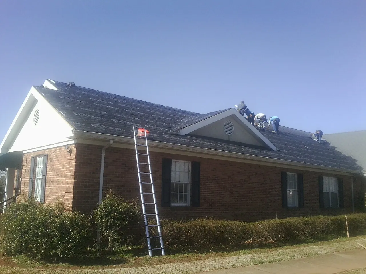 Crew tearing shingles off a brick ranch roof with a ladder set — Metal Roof Repair work by our crew in Bullard
