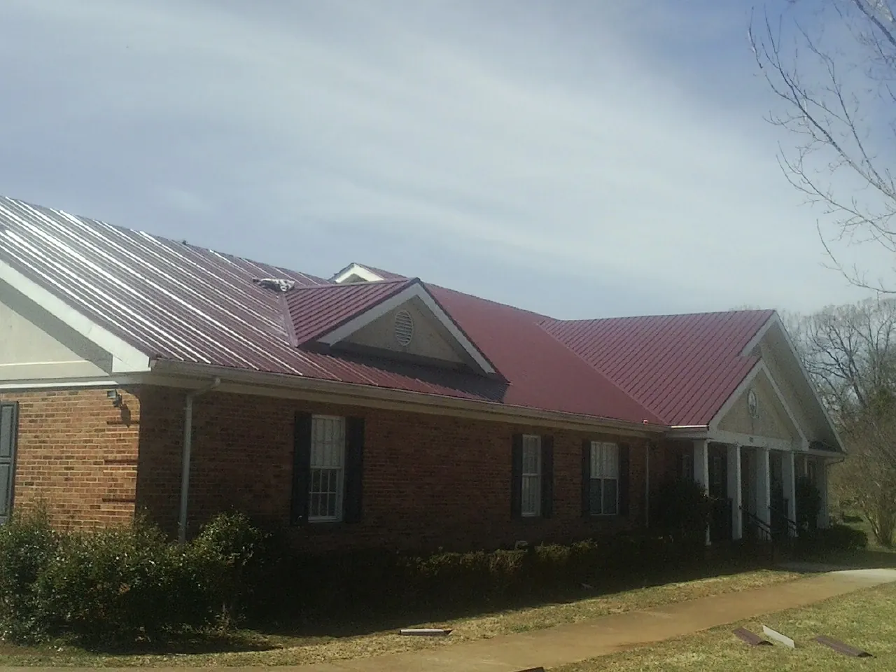 Red metal roof with gabled entries on a long brick building, from a Hail Damage Roof Repair job in Bullard