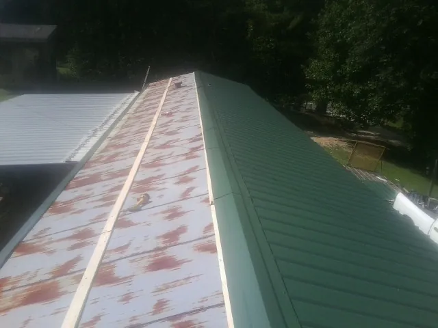 Old rusted panels beside newly installed green metal roofing — Wind Damage Roof Repair by Roofing Brothers in Bullard