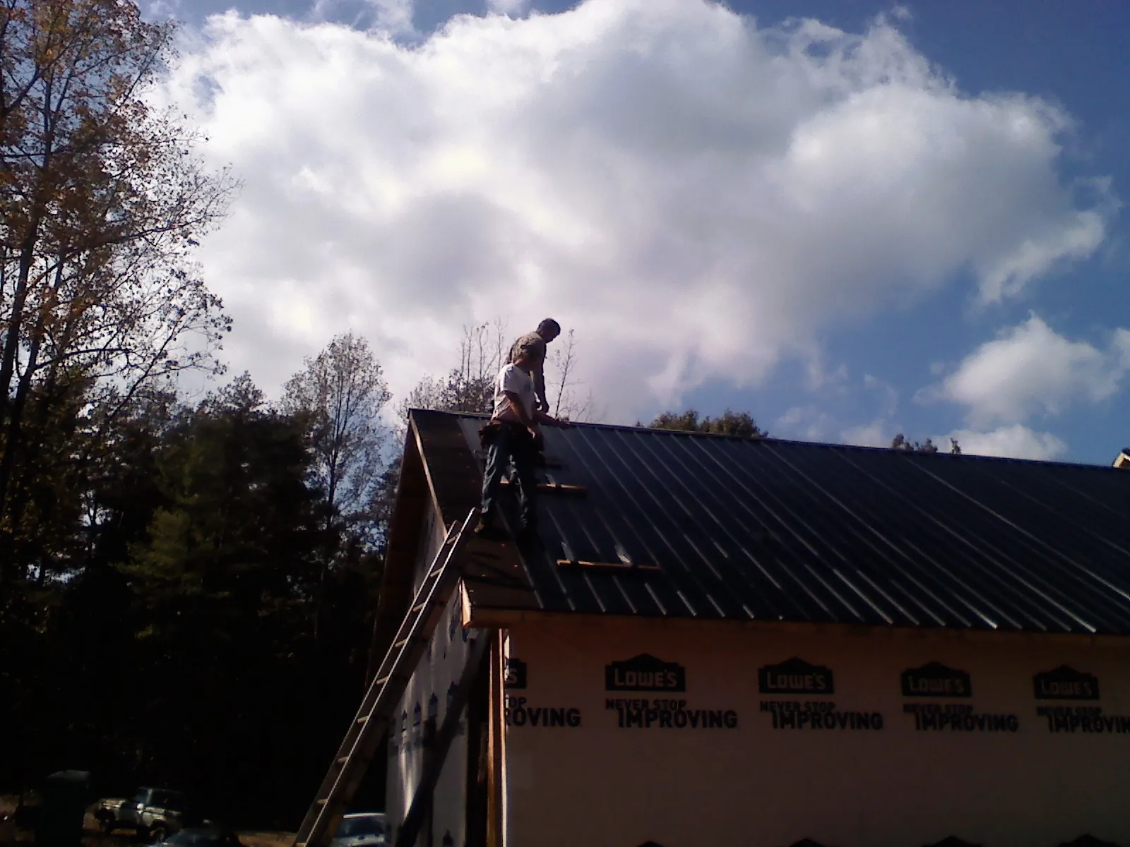 Roofer fastening dark metal panels high against a cloudy sky, from a Roof Inspection job in Bullard