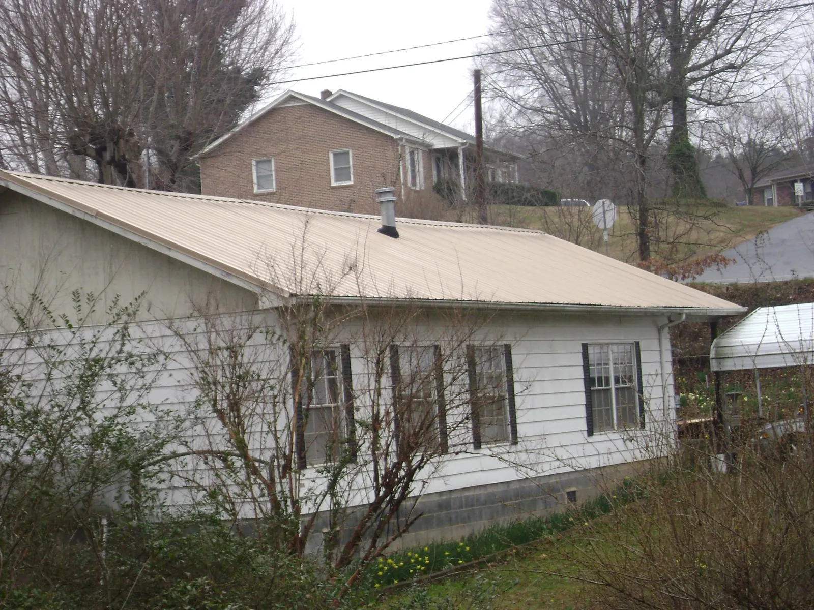 Tan metal roof on a white sided house set into a hillside — Commercial Roofing by Roofing Brothers in Bullard