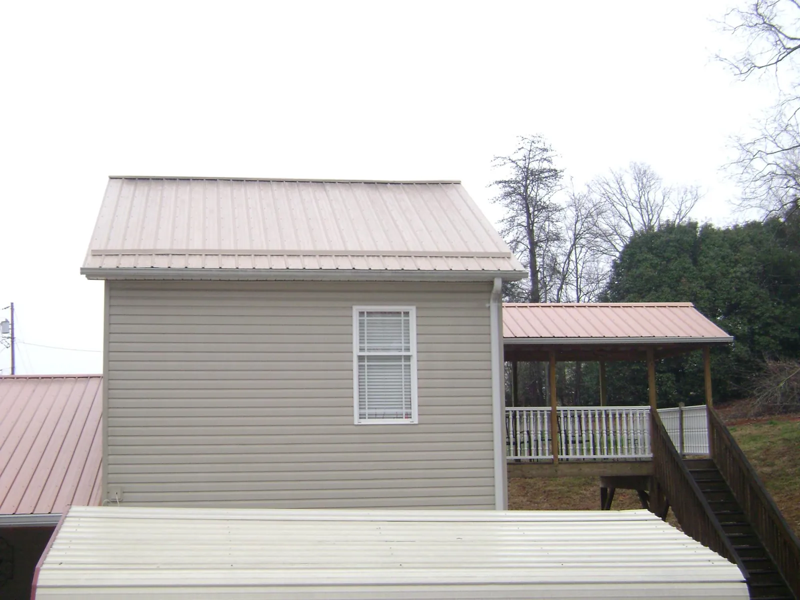 Tan metal roofs on a two story addition and attached porch, from a Roof Replacement job in Bullard
