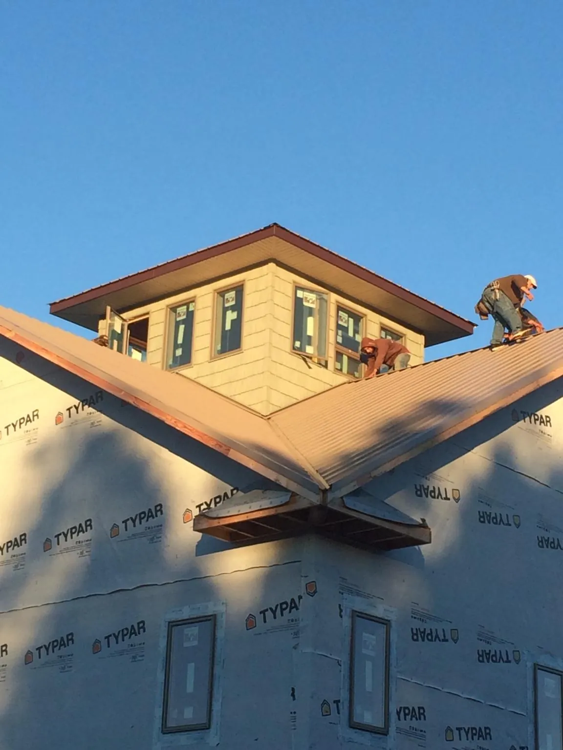 Roofers working around a rooftop cupola on a new metal roof at sunset in Bullard